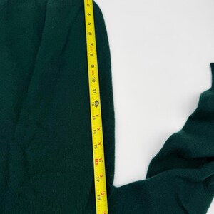 Puede incluir: Una prenda de punto de color verde oscuro con cintura acanalada, colocada junto a una cinta m&eacute;trica amarilla que indica una longitud de aproximadamente 51 cm desde el borde superior hasta el dobladillo inferior visible.