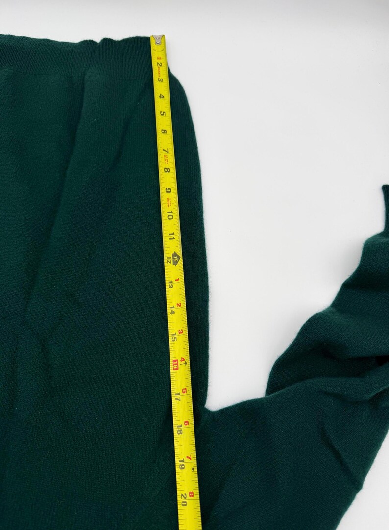 Puede incluir: Una prenda de punto de color verde oscuro con cintura acanalada, colocada junto a una cinta m&eacute;trica amarilla que indica una longitud de aproximadamente 51 cm desde el borde superior hasta el dobladillo inferior visible.