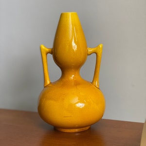 May include: A yellow ceramic vase with two handles. The vase has a bulbous shape and a glossy finish.