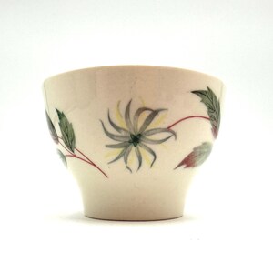 May include: Cream-colored ceramic bowl with a floral design. The bowl features a hand-painted flower with gray, yellow, and green details, along with green and red leaves. The bowl has a slightly flared shape.
