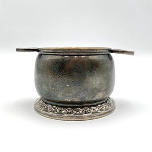 May include: A silver-plated sugar bowl with a lid and two handles. The bowl has a decorative base with a scalloped design.