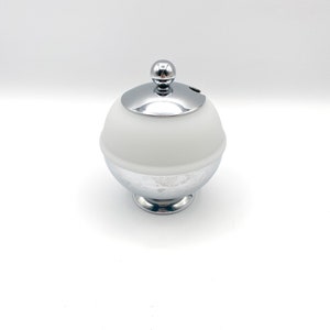 May include: A white ceramic sugar bowl with a chrome lid and base. The lid has a small knob on top.