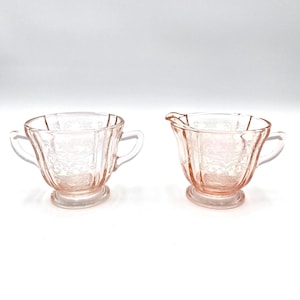 May include: A set of two vintage pink glass sugar and creamer. The sugar bowl and creamer have a delicate floral pattern and are in excellent condition.