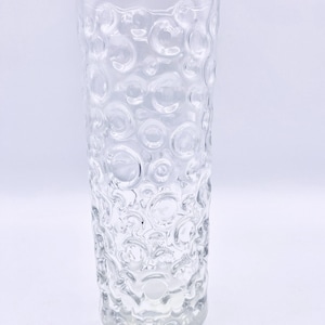 May include: A clear glass vase with a textured surface. The vase has a cylindrical shape and is decorated with a pattern of small, raised circles.