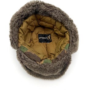 May include: A brown trapper hat with a thick, fuzzy faux fur lining and a quilted tan interior. The hat features a camouflage pattern on the outer band and a black label inside with the text Browning Down and a buck logo, stating Made in USA.