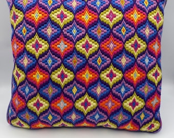May include: A colorful pillow with a geometric pattern in shades of purple, blue, yellow, orange, and pink. The pillow is made of a soft, textured fabric and has a rectangular shape.