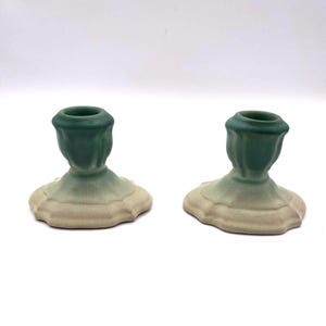 May include: A pair of green and white ceramic candle holders. The holders have a scalloped base and a fluted design.