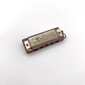 May include: A small, silver harmonica with a red plastic case. The harmonica has the words "Little Lassie" engraved on the top.