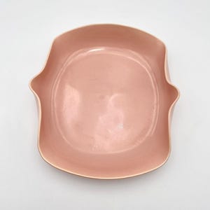 May include: A light pink ceramic serving bowl with a unique, wavy rim. The bowl is smooth and glossy.