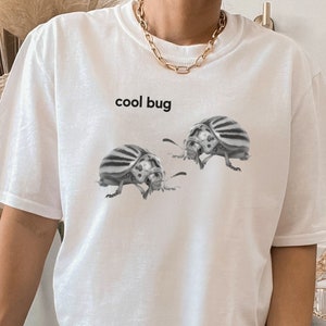 May include: White t-shirt with the text "cool bug" printed on the front. Two black and white beetle illustrations are below the text.