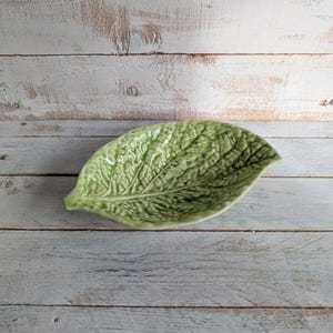 May include: A green ceramic leaf-shaped serving dish. The dish is designed to look like a cabbage leaf with a textured surface.