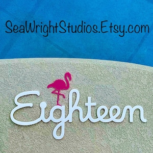 May include: White cursive text that says "Eighteen" with a pink flamingo silhouette above the word. The background is a light beige with a textured surface.