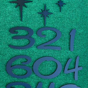 May include: Black metal numbers and stars on a green background. The numbers are 3, 2, 1, 6, 0, 4, 3, 1, 1, and 0.