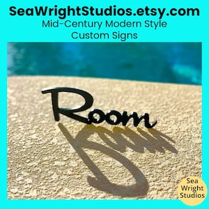 May include: Black metal sign with the word "Room" in a modern font. The sign is sitting on a light beige surface with a shadow cast from the sign.