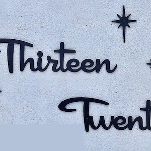 May include: Black metal cutout of the words "Thirteen" and "Twenty" with a star design on a white wall.