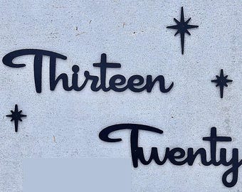 May include: Black metal cutout of the words "Thirteen" and "Twenty" with a star design on a white wall.