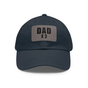 May include: A navy blue baseball cap with a gray patch that says "DAD X3" in black text.