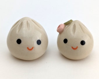 Dos adorables dumplings de cerámica hechos a mano: uno con flor. Dumplings de sopa alegres. Xiao long bao. Cerámica de producción artesanal. Cerámica pintada a mano.