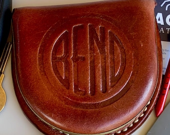 Könnte beinhalten: Ein brauner Golf-Putter-Schlägerhaube aus Leder in abgerundeter Form mit einem geprägten kreisförmigen Logo, das in der Mitte das Wort BEND zeigt. Die Hülle hat sichtbare helle Nähte entlang der Unterkante und eine glatte, polierte Lederoberfläche.