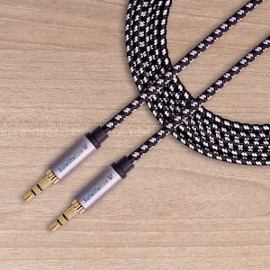 May include: Two audio cables with gold connectors and grey metal housings. The cables are black and white braided, with the text "SatelliteSale" printed on the housings. The background is a light brown wooden surface.