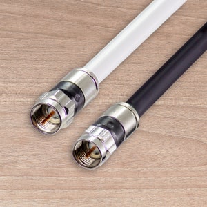 May include: Two coaxial cables, one white and one black, with silver connectors. The cables are angled against a light brown wood-grain background. The connectors have a threaded design.