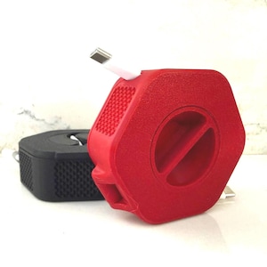 May include: A red and black hexagonal cable organizer with a white cable extending from the red organizer. The red organizer has a textured surface and a circular opening. The black organizer is in the background.
