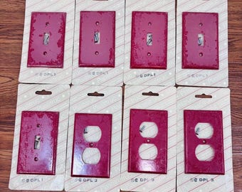 May include: Eight red plastic wall plates with a textured finish. Four plates are for single light switches and four plates are for electrical outlets. Each plate has the text "DPL1" or "DPL3" printed on the bottom.