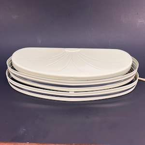May include: A vintage, off-white, semi-circular light fixture. The fixture has a decorative, fan-shaped design on the top and is surrounded by a series of curved, parallel metal bands. A power cord extends from the side.
