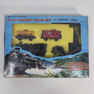 May include: A vintage No. 87 Freight Train Set in a blue box. The set includes a black locomotive, a red caboose with "NYC" text, and a yellow tanker car with "SHELL" text. The box art shows a train on a track with a bridge.