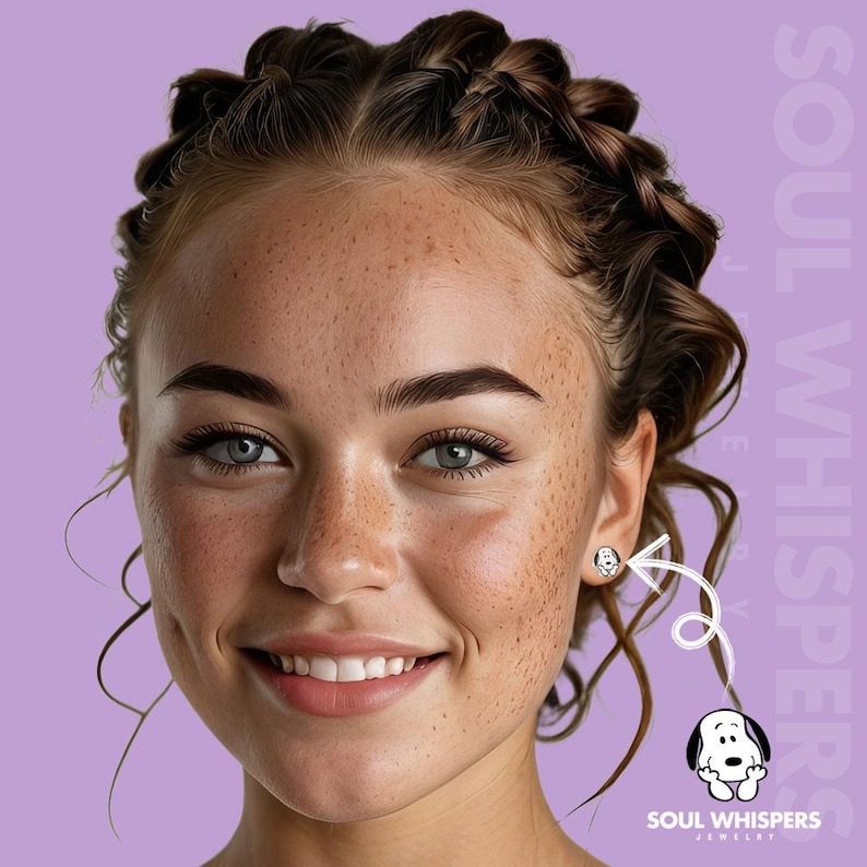 May include: A woman with freckles smiles, wearing a Snoopy stud earring. The earring is white with a black outline of Snoopy's face. The background is a light purple color with the words "SOUL WHISPERS JEWELRY".