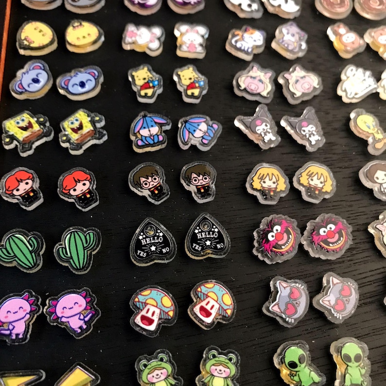 May include: A collection of clear, resin-like charms with various cartoon and character designs. The charms feature images of koalas, Winnie the Pooh, SpongeBob, Harry Potter, and more. Some charms have the text "HELLO YES NO".