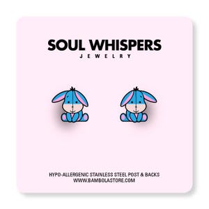 May include: A pair of cartoon-style earrings featuring a blue donkey character with pink accents. The earrings are on a pink background with the text "SOUL WHISPERS JEWELRY". The earrings have hypo-allergenic stainless steel posts and backs.