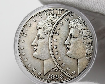 Op de afbeelding: Een zilveren munt met twee profielen van een vrouw, de woorden "E PLURIBUS UNUM" en "LIBERTY" zijn zichtbaar. Het jaartal "1893" is ook weergegeven. De munt zit in een doorzichtige plastic houder.