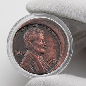 Może przedstawiać: Moneta Lincoln z 1955 roku w kolorze miedzi, umieszczona w przezroczystym plastikowym etui. Na monecie widnieje profil Abrahama Lincolna z napisem "IN GOD WE TRUST" i "LIBERTY".