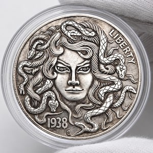 May include: A silver-toned circular coin featuring a relief portrait of a figure with snakes for hair. The word LIBERTY is inscribed on the upper right side, and the year 1938 is embossed on the lower left side. The coin is encased in a clear plastic capsule.