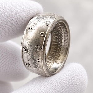 Peut inclure: Une bague en forme de pièce de monnaie argentée fabriquée à partir d'une pièce américaine de 1964. La surface extérieure présente le texte "IN GOD WE TRUST" et l'année "1964" en relief. Le bord intérieur affiche le texte "UNITED STATES OF AMERICA".