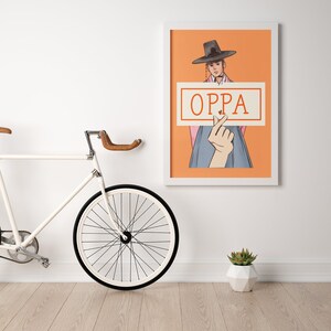 May include: A framed art print featuring a stylized illustration of a person in traditional Korean attire holding a sign that reads "OPPA" with a heart symbol. The artwork is set against an orange background.
