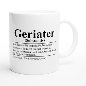 Könnte beinhalten: Weiße Keramiktasse mit einem schwarz-weißen Design. Die Tasse zeigt das Wort "Geriater" definiert als "eine Person, die ständig Probleme löst, von denen man nicht einmal wusste, dass sie existieren, auf eine Art und Weise, die man nicht versteht." Der Text enthält auch "(Substantiv)" und "(Siehe auch: Held, Vorbild, Genie)".