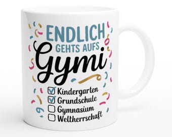 Könnte beinhalten: Weiße Keramik-Tasse mit dem Text "ENDLICH GEHTS AUFS Gymi" in blauer und schwarzer Schrift, mit Konfetti-ähnlichen Dekorationen. Die Tasse hat einen Henkel und Kontrollkästchen für Kindergarten, Grundschule, Gymnasium und Weltherrschaft.