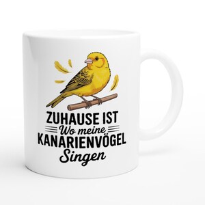 Könnte beinhalten: Eine weiße Keramiktasse mit einem gelben Kanarienvogel, der auf einem braunen Ast sitzt, umgeben von einzelnen Federn. Unter dem Vogel steht in schwarzer Schrift: ZUHAUSE IST Wo meine KANARIENVÖGEL Singen. Das Motiv ist mittig auf der Tasse platziert.