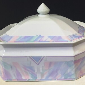 May include: White ceramic serving dish with lid. The dish has an octagonal shape and is decorated with pastel watercolor-like patterns in shades of blue, purple, and pink. It features two handles and a decorative finial on the lid.