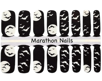 May include: Black nail wraps with a Halloween theme. Each wrap features a black background with white bats and a white moon. The text "Marathon Nails" is printed on the wraps.