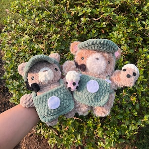 Puede incluir: Dos osos de peluche que llevan monos verdes y marrones con detalles blancos. Los osos sostienen pequeñas tazas con diseños rosas y blancos.