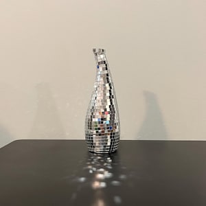 May include: A silver vase with a mirrored mosaic design. The vase has a long, narrow neck and a rounded base.