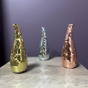 May include: Three decorative vases with a mosaic tile design. The vases are gold, silver, and rose gold.