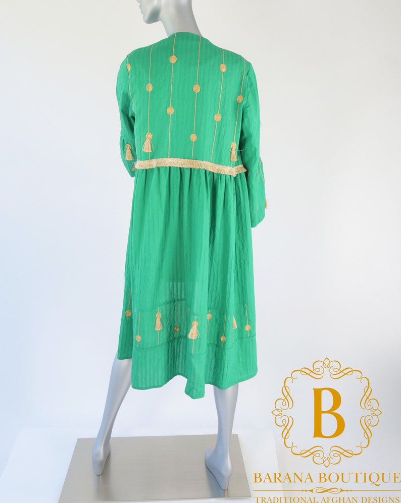 May include: A green dress with gold embroidery and tassels. The dress has a round neckline and a loose fit. It is made of a lightweight fabric and has a flowing silhouette.