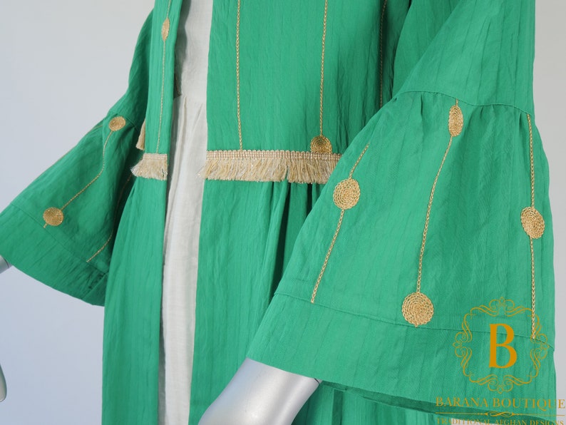 May include: A green long-sleeved cardigan with gold embroidery and fringe trim. The cardigan has a loose fit and a flowy silhouette.