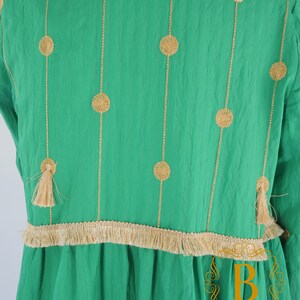 May include: A green dress with gold embroidery and a fringe trim. The embroidery features a repeating pattern of circles.