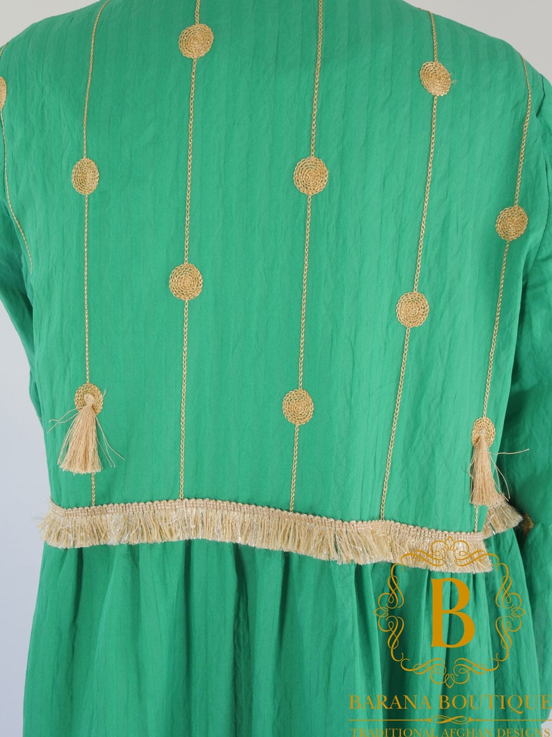 May include: A green dress with gold embroidery and a fringe trim. The embroidery features a repeating pattern of circles.