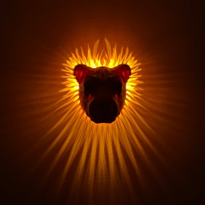 May include: A paper lampshade shaped like a bear's head with a light shining through the paper, creating a warm glow. The lampshade is lit and casts a shadow of a bear's head on the wall.